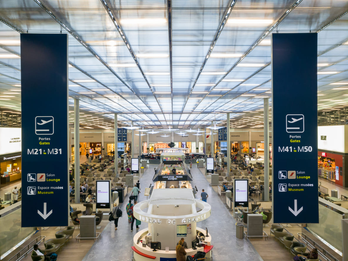 A bustling interior of Paris Charles de Gaulle Airport featuring spacious seating, shopping outlets, and clear signage for travelers.