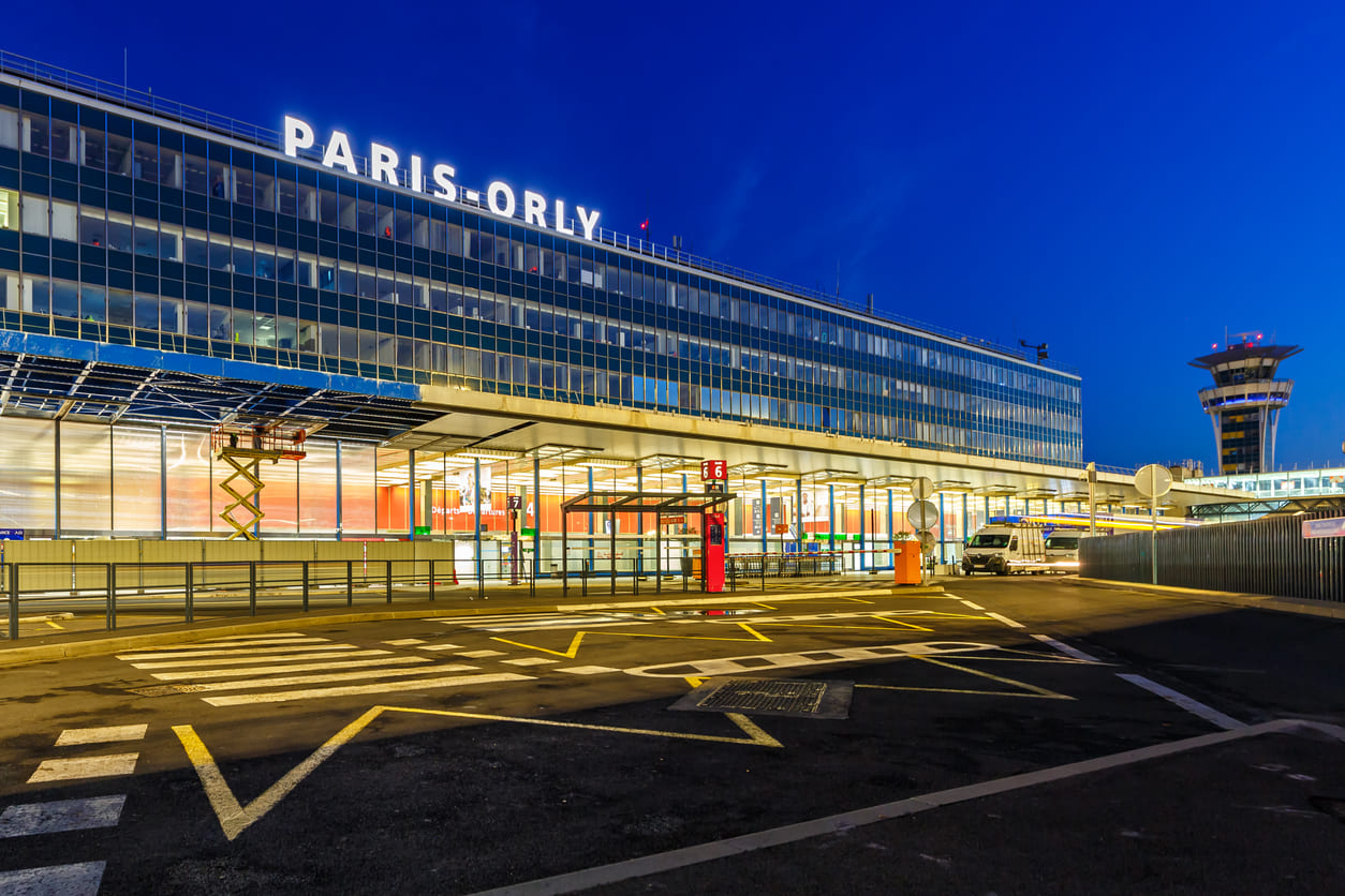 A nighttime view of Paris-Orly Airport featuring its illuminated modern facade, clear signage, and prominent control tower.