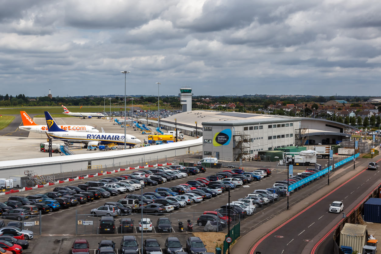London Southend Airport's terminal with Ryanair and easyJet planes on the tarmac, alongside a bustling parking area.