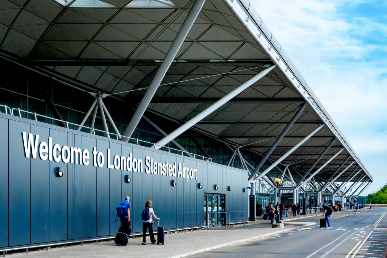 The modern entrance of London Stansted Airport, with travelers entering.