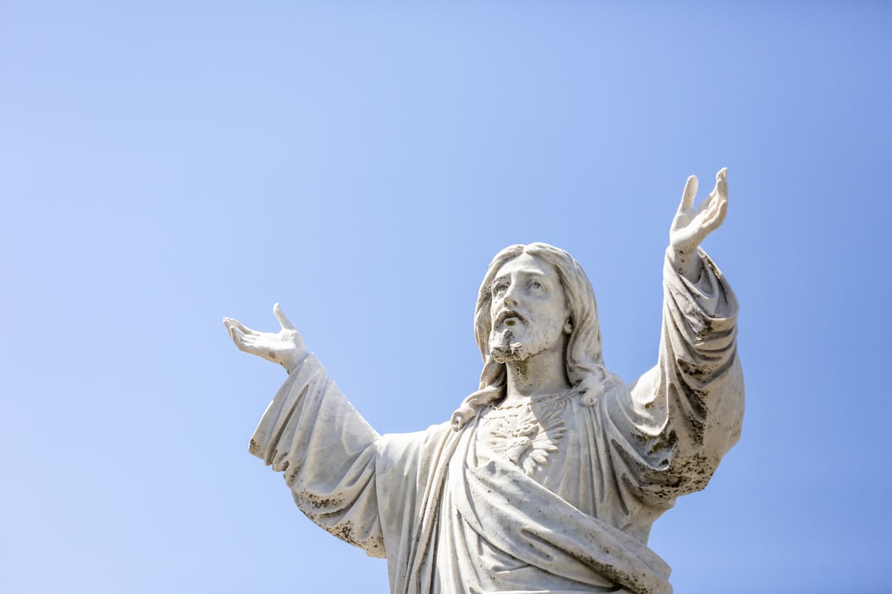 A white statue of Jesus with outstretched arms stands against a clear blue sky, symbolising his ascension into heaven.