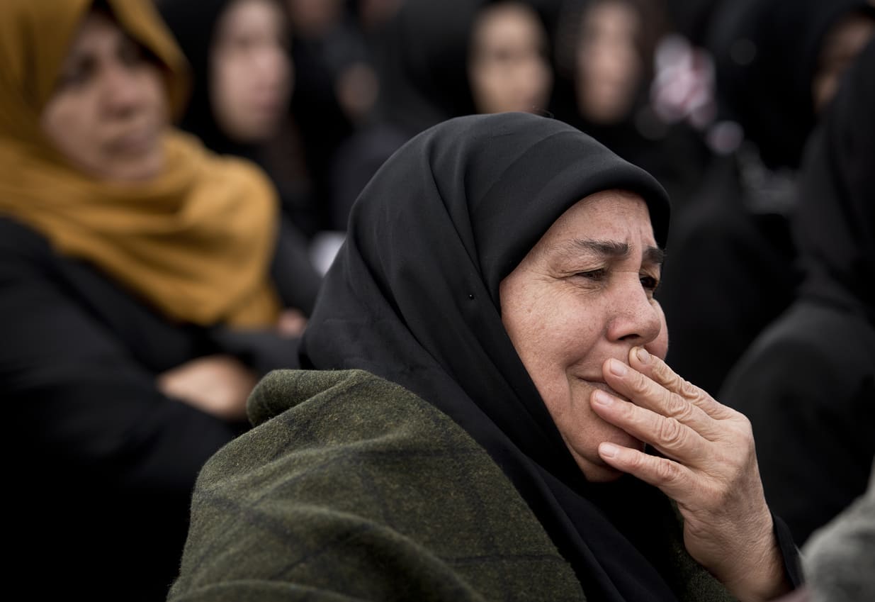 A woman in a black headscarf, visibly emotional, surrounded by others in mourning during an Ashura gathering.