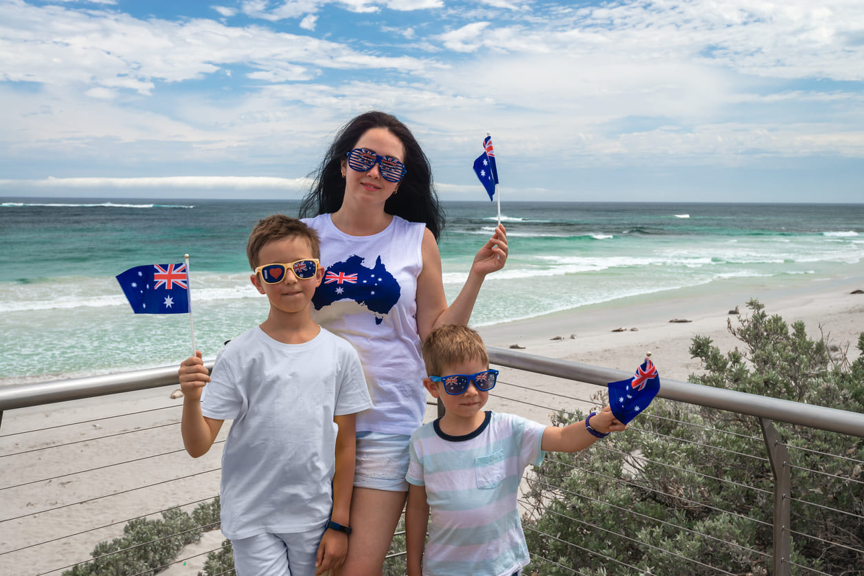 A family dressed in Australian-themed attire waves flags by the beach, celebrating Australia Day with national pride and summer festivities.