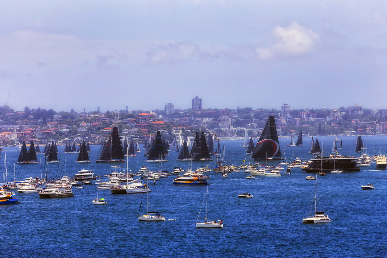 A fleet of yachts sets sail from Sydney Harbour on Boxing Day, kicking off the world-famous Sydney to Hobart Yacht Race amid a vibrant celebration.