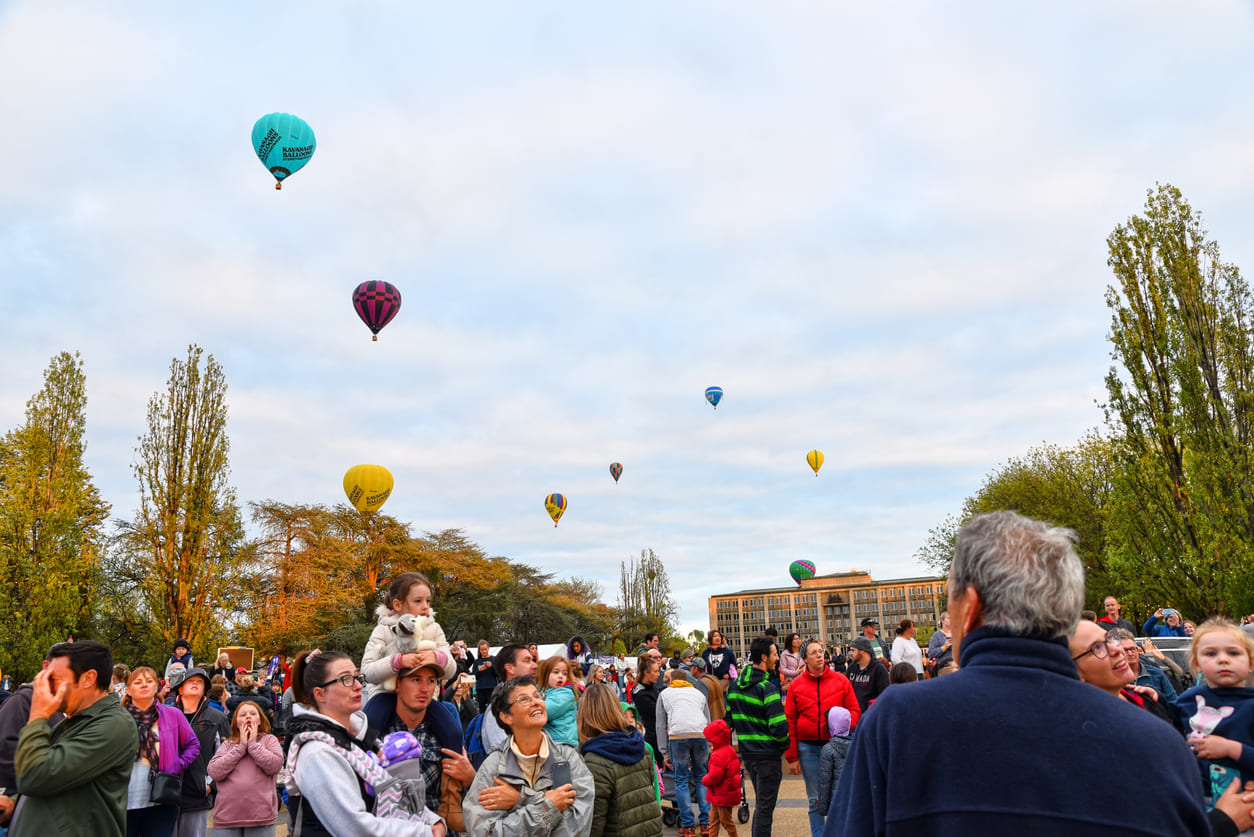 A lively crowd gathered beneath a sky filled with colorful hot air balloons, capturing the festive atmosphere of Canberra Day.