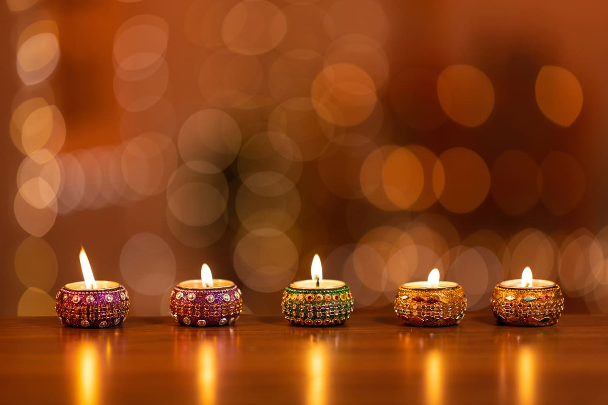 A row of ornate, beaded oil lamps glowing softly against a warm, blurred background, evoking the essence of Diwali.