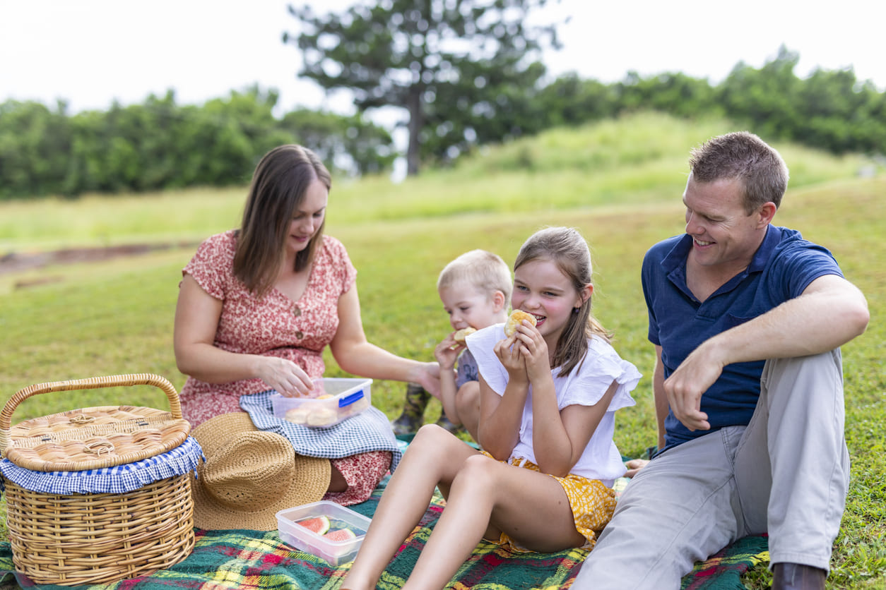 A cheerful family sharing food and laughter during a picnic on a grassy field, enjoying the Easter holiday together.