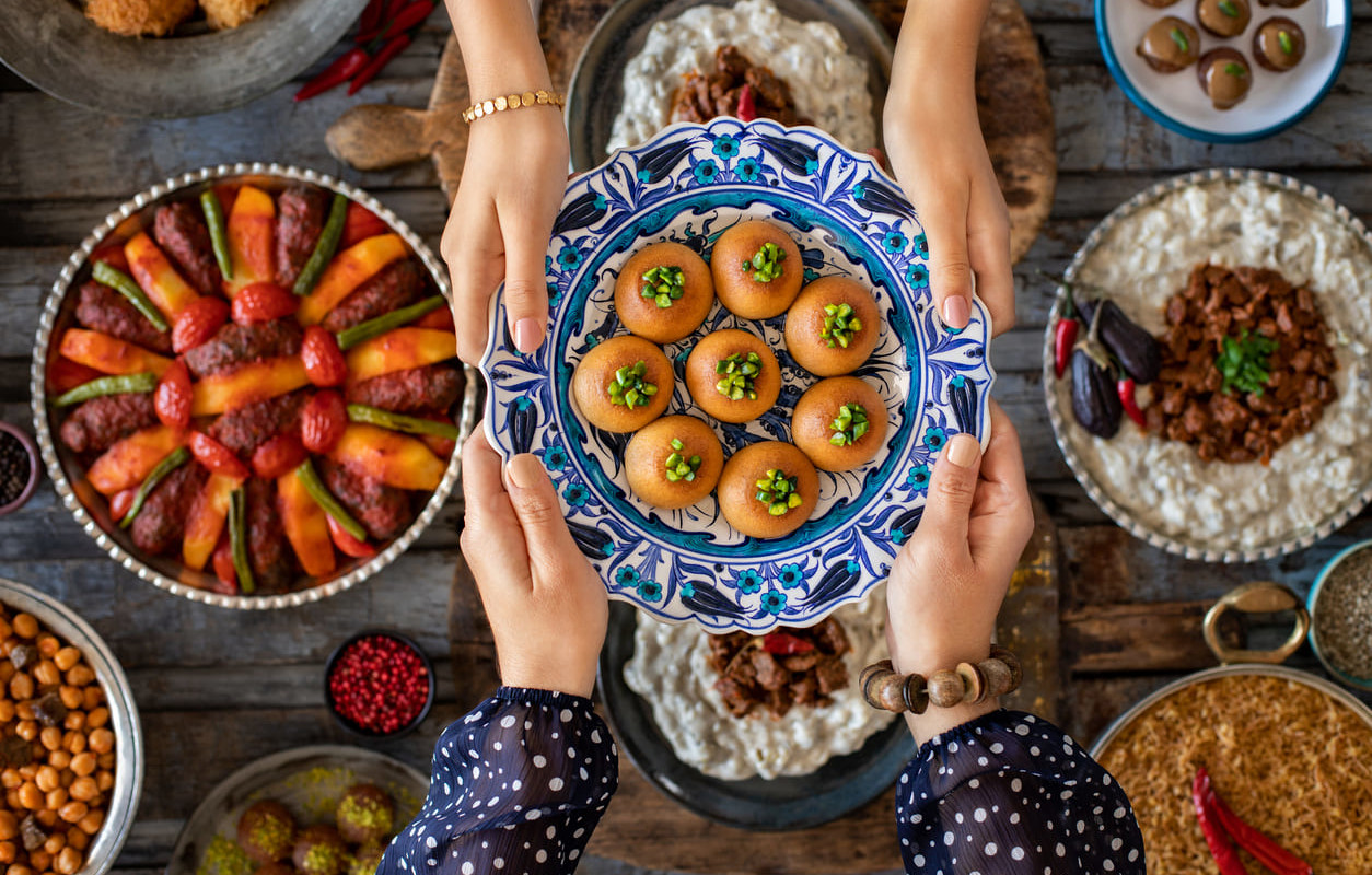 A beautifully arranged table of traditional dishes and sweets, with hands sharing a decorative plate of treats, symbolizing festivity and togetherness.