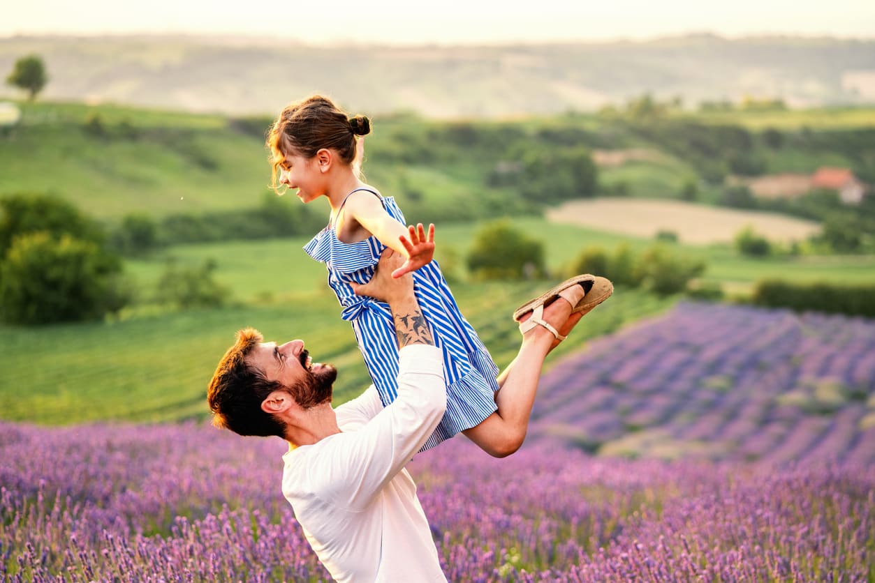 A father joyfully lifts his daughter in a scenic lavender field, capturing a heartwarming Father's Day moment filled with love and happiness.