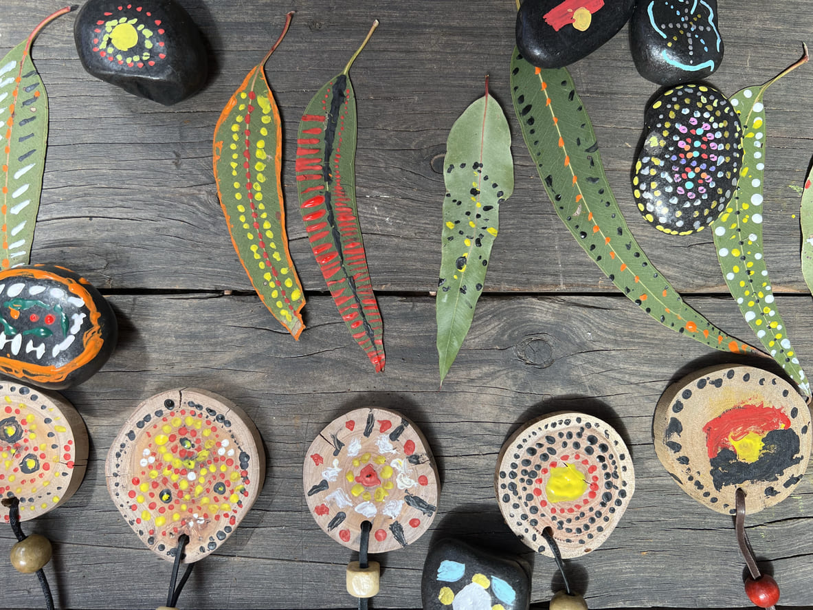 A colorful arrangement of hand-painted eucalyptus leaves, stones, and wooden medallions created during NAIDOC Week to celebrate Indigenous culture.