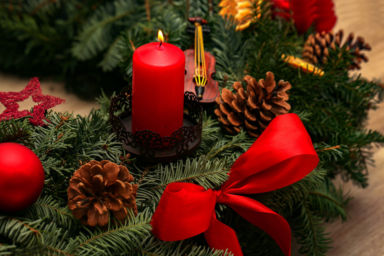 An Advent wreath adorned with a glowing red candle, pine branches, pinecones, and festive decorations, symbolizing hope and the start of the Christmas season.