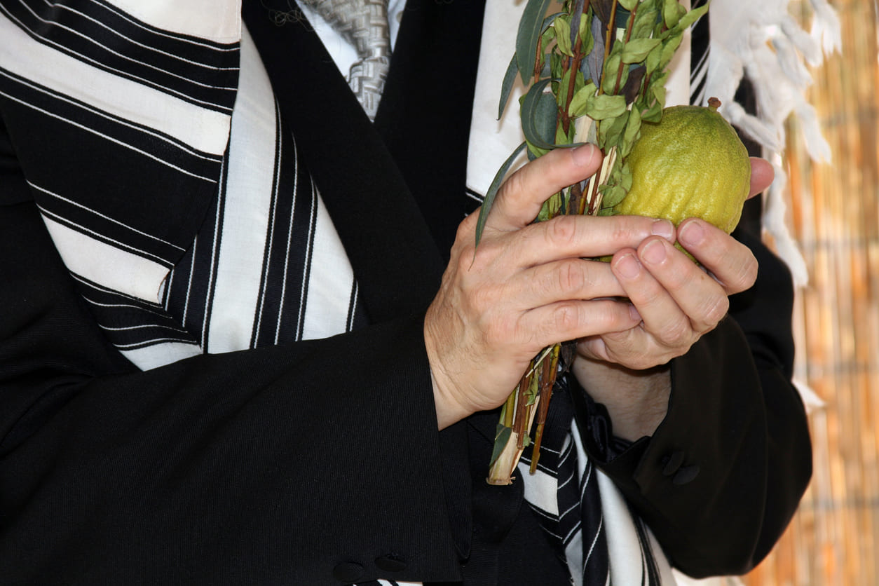 A close-up of a person holding the lulav and etrog during Hoshana Rabbah, wrapped in a traditional prayer shawl.