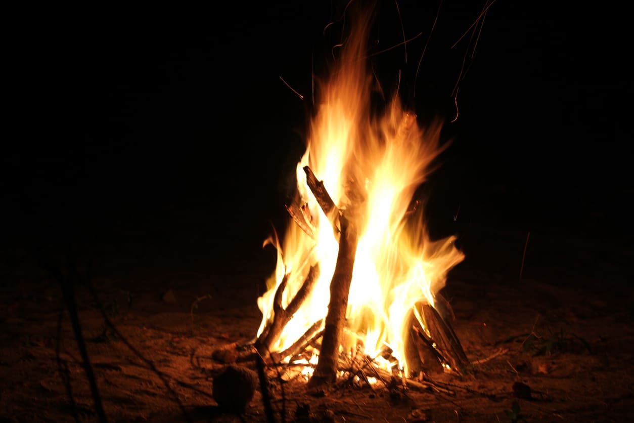 A bright bonfire burns on sandy ground under the night sky, creating a warm and festive atmosphere.