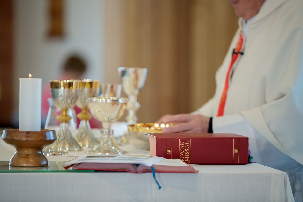 A priest at the altar with chalices, a candle, and the Roman Missal during a Maundy Thursday service.