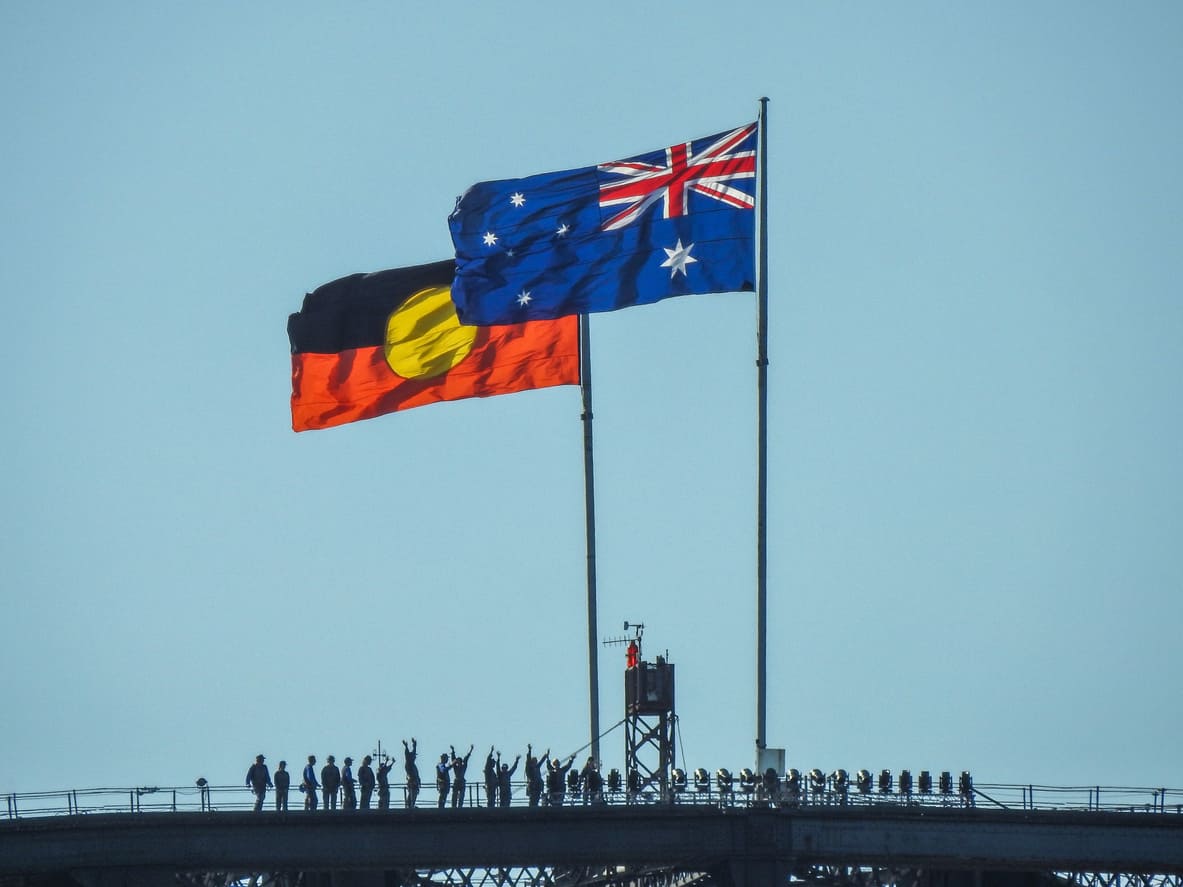 The Aboriginal and Australian flags wave side by side atop a bridge, symbolizing unity, recognition, and reconciliation.