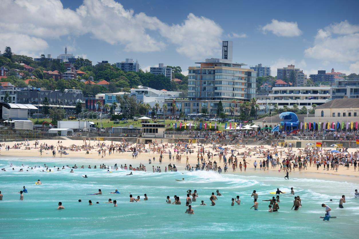 A bustling Australian beach on New Year's Day, filled with people enjoying the summer sun, swimming, and celebrating the start of the year.