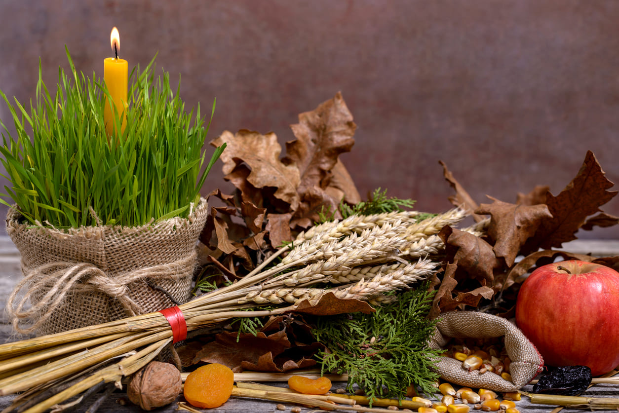 A rustic display of traditional Orthodox Christmas Eve symbols, including green wheat with a candle, dried fruits, grains, and a yule log.