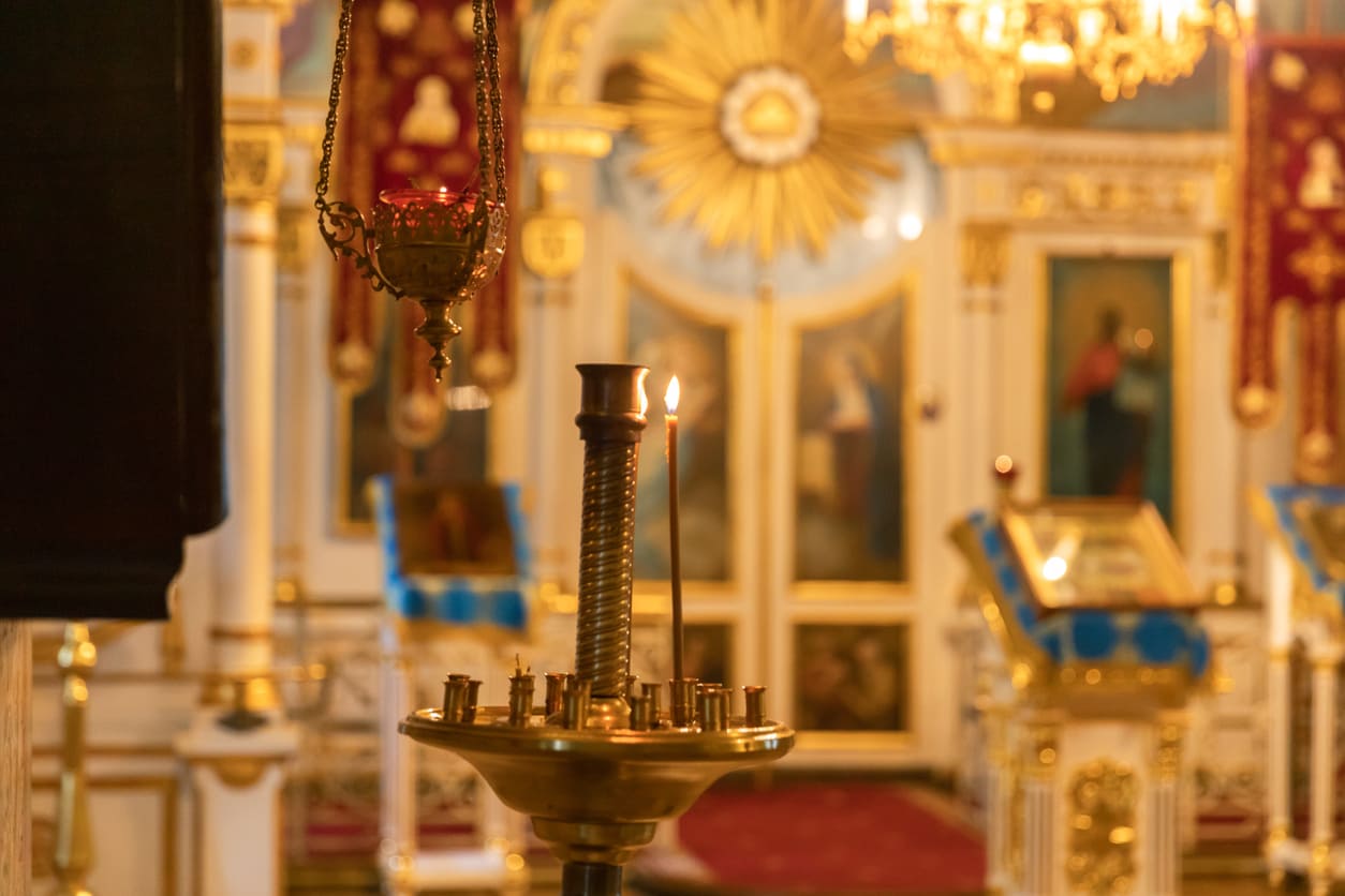 A softly lit Orthodox church interior with a single candle glowing, symbolizing the solemn and sacred atmosphere of Holy Saturday.