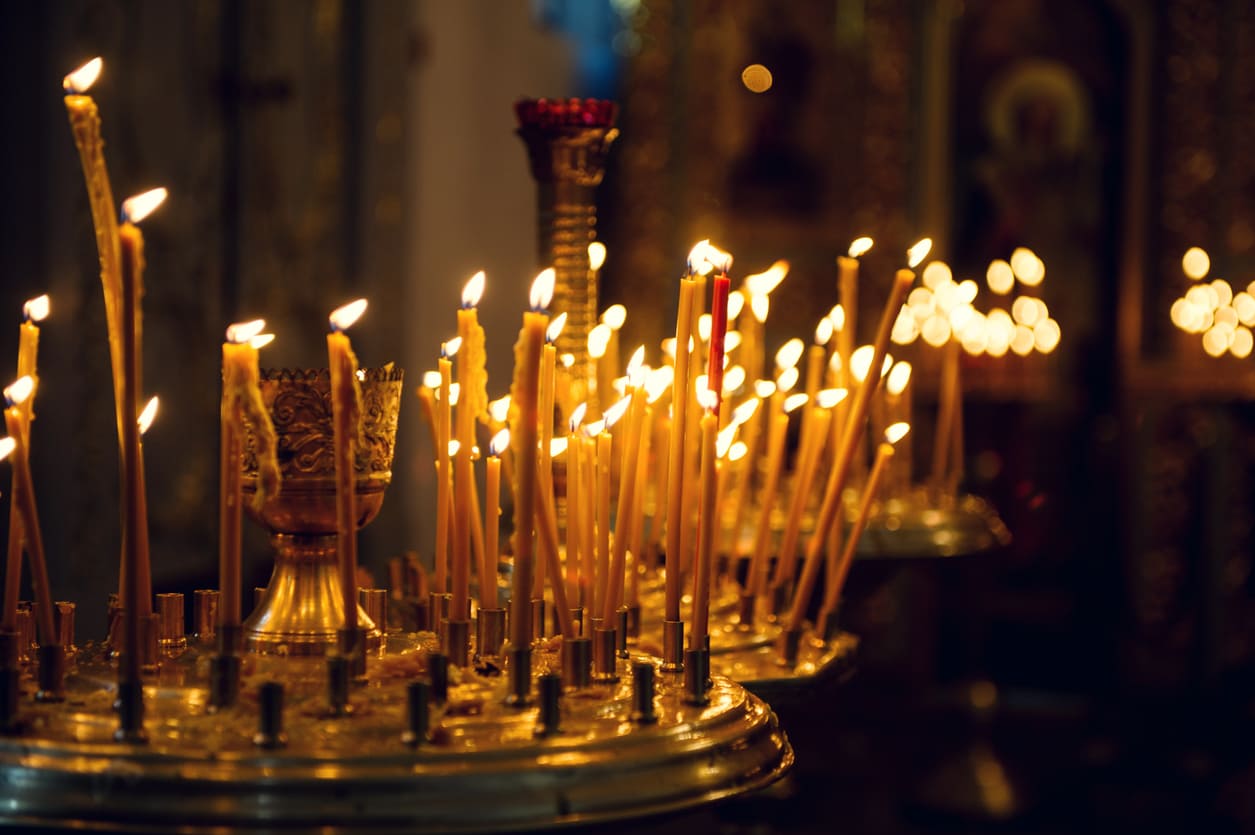 Rows of slender candles glowing softly in an ornate Orthodox church setting, creating a warm and reverent atmosphere.