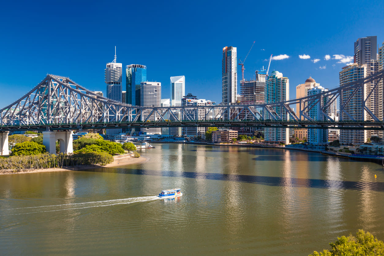 Brisbane's Story Bridge spanning the river, with the city skyline rising behind it under a clear blue sky.