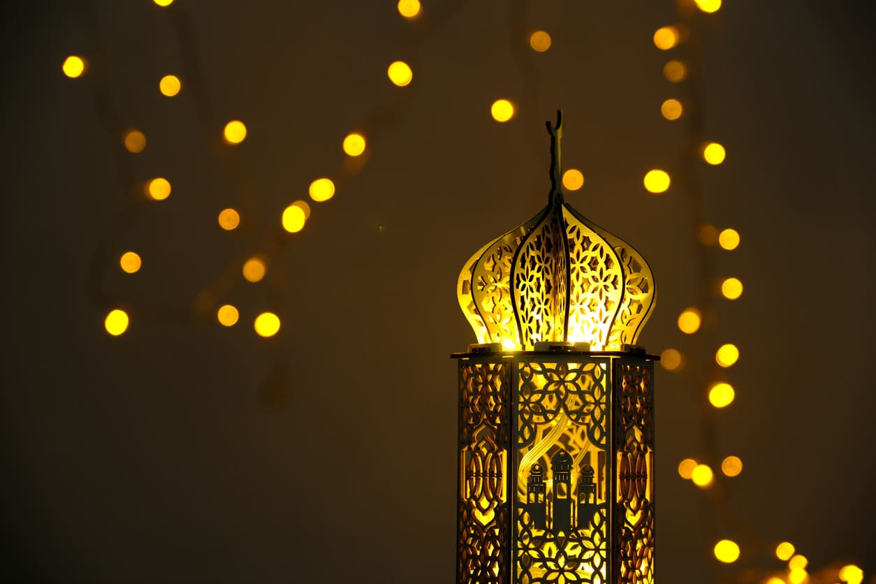 An ornate, golden lantern illuminated against a dark background, surrounded by soft, glowing fairy lights.