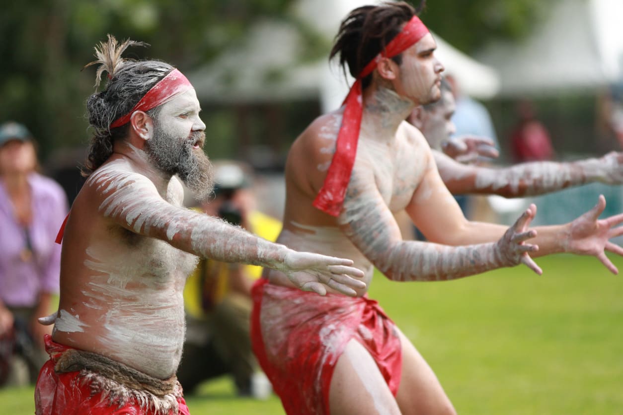 Aboriginal men in traditional attire and body paint performing a cultural dance during a public celebration.
