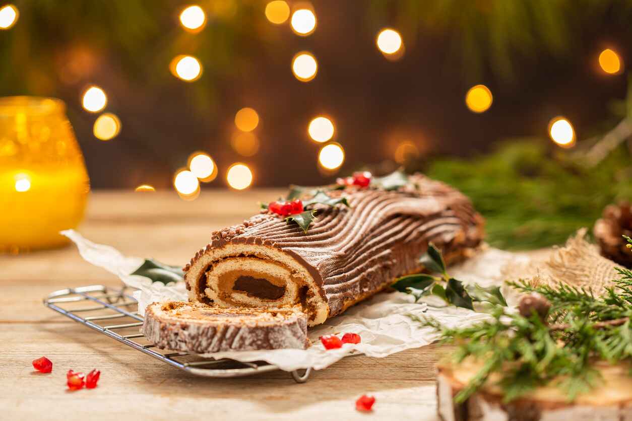 A beautifully decorated Yule log cake with chocolate frosting and festive garnishes, set against a warm, glowing holiday backdrop.