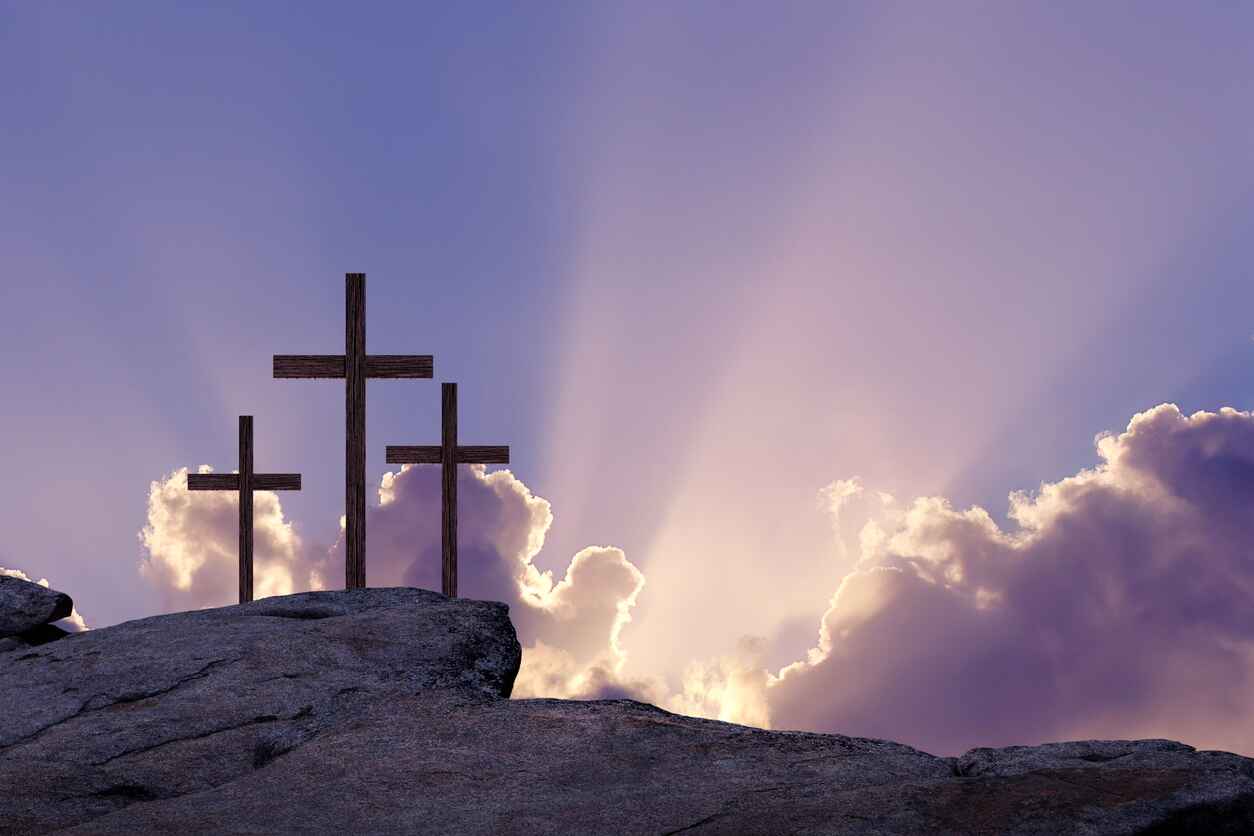 Three wooden crosses stand on a rocky hill, illuminated by rays of light breaking through the clouds, symbolizing the crucifixion and remembrance of Good Friday.