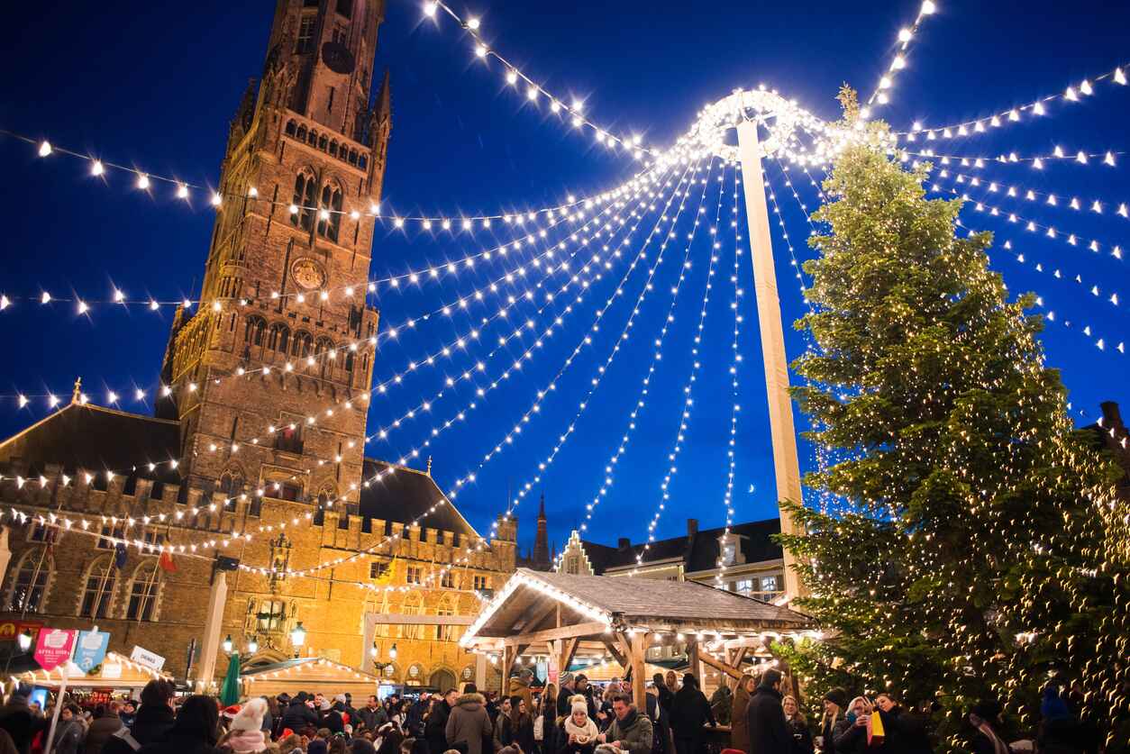 A vibrant Christmas market in Belgium, illuminated by festive lights, with a towering Christmas tree and joyful crowds celebrating the holiday season.