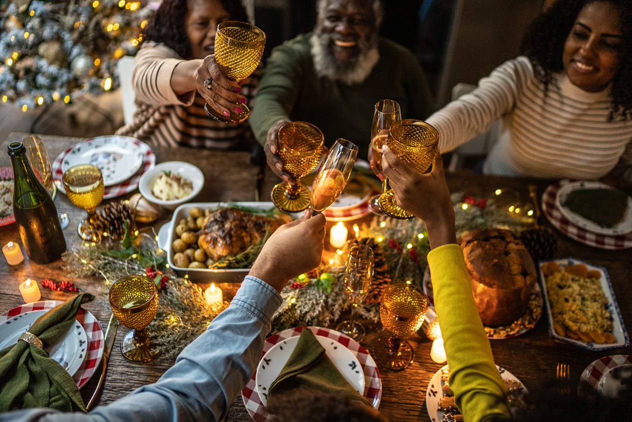 A warmly lit dinner table where family members raise their glasses in a cheerful toast, surrounded by festive food, candles, and Christmas decorations.
