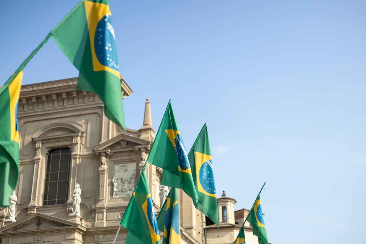 Several Brazilian flags waving in front of a historic building under a clear blue sky, reflecting a patriotic and festive scene.