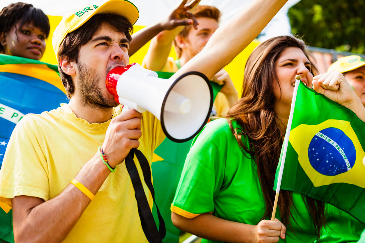 A lively crowd holding Brazilian flags and a megaphone, gathered in solidarity to support and advocate for workers' rights on Labor Day.