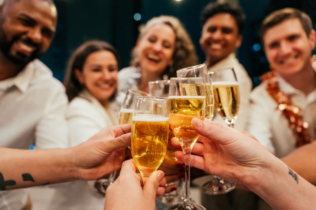 A group of smiling friends clinking glasses filled with sparkling drinks, dressed festively and celebrating together on New Year's Eve.