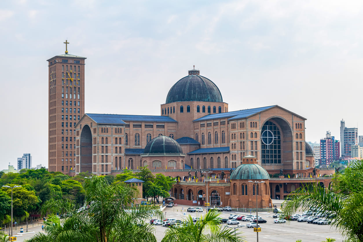 A grand view of the Basilica of Our Lady of Aparecida, featuring its towering dome and impressive architecture, surrounded by greenery and city buildings.