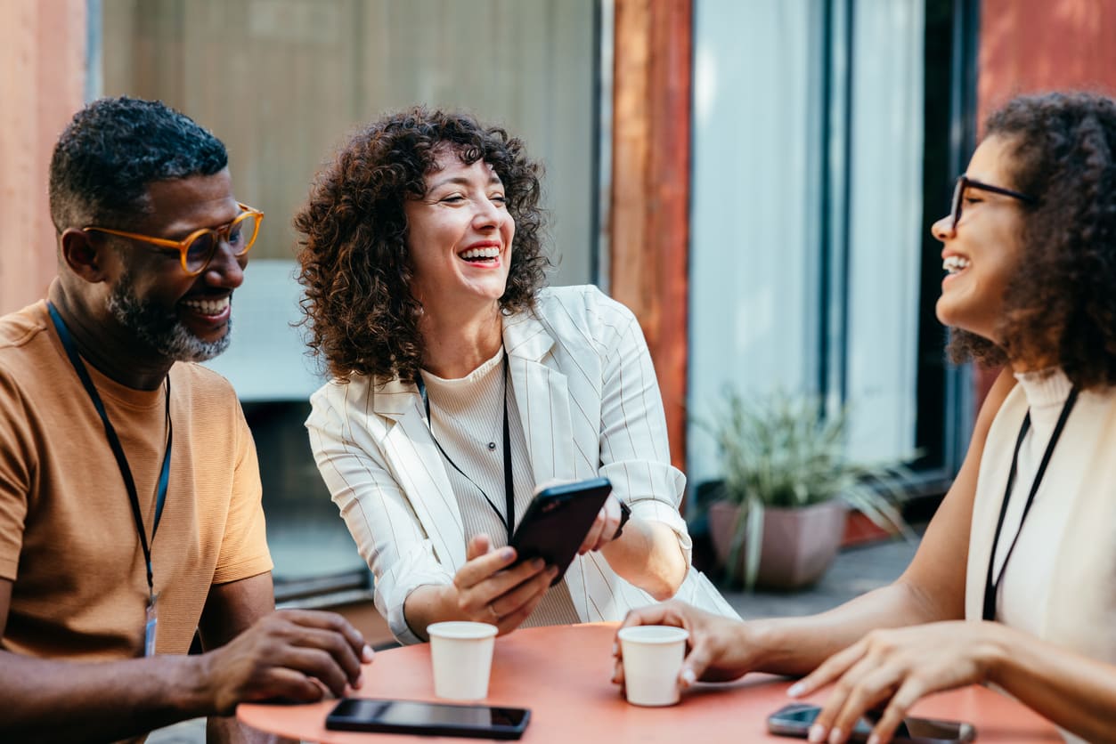 Three colleagues sit around a table, laughing and enjoying a light-hearted conversation over coffee.