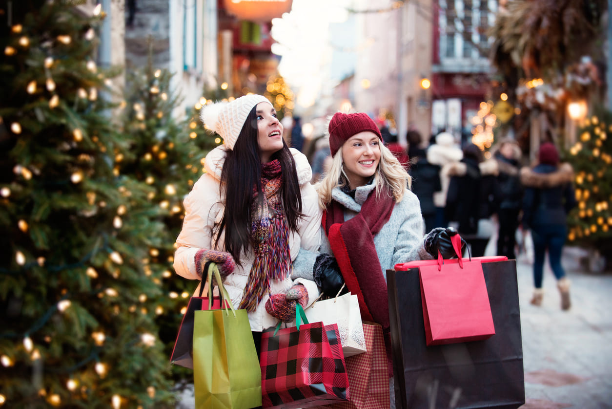 Two joyful shoppers walking through a beautifully decorated winter street, carrying bags filled with Boxing Day deals and holiday cheer.