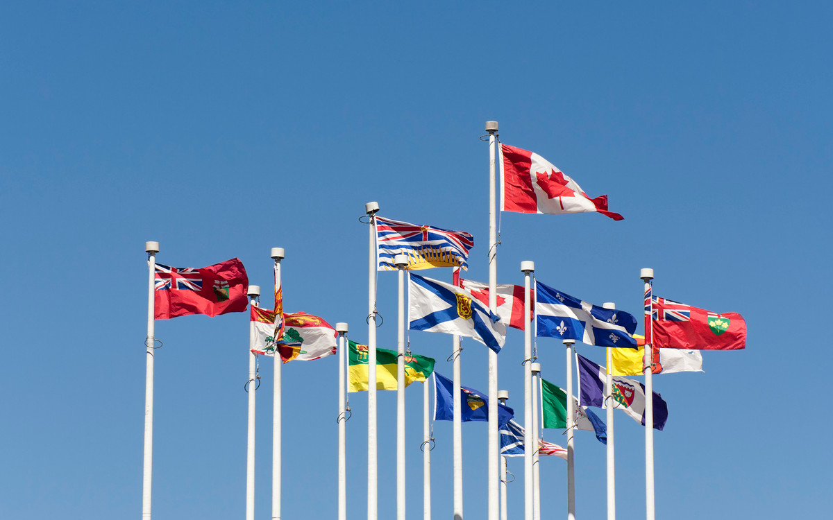 A collection of Canadian provincial and territorial flags waving against a clear blue sky, representing the diverse regional celebrations of Civic Holiday.