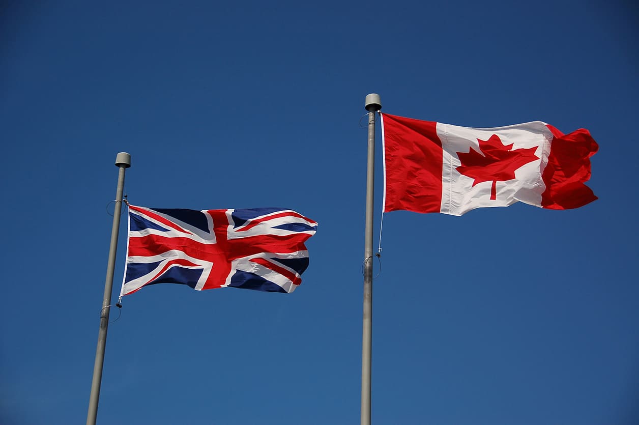 The Canadian and British flags fly together against a clear blue sky, representing their historical connection through the Commonwealth of Nations.