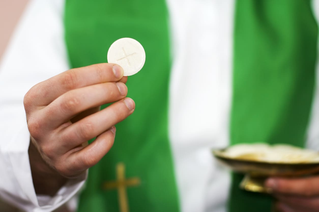 A priest holding the Eucharist, representing the sacred ritual of Communion during Corpus Christi celebrations.