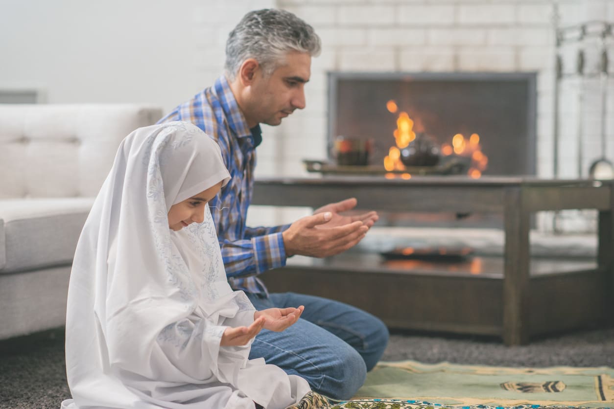 A father and daughter sit in prayer, embracing the spiritual essence of Eid al-Adha in a warm and peaceful home setting.