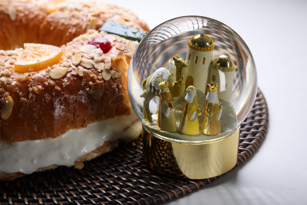 A traditional King's Cake alongside a decorative snow globe featuring the Three Wise Men, symbolizing the celebration of Epiphany.