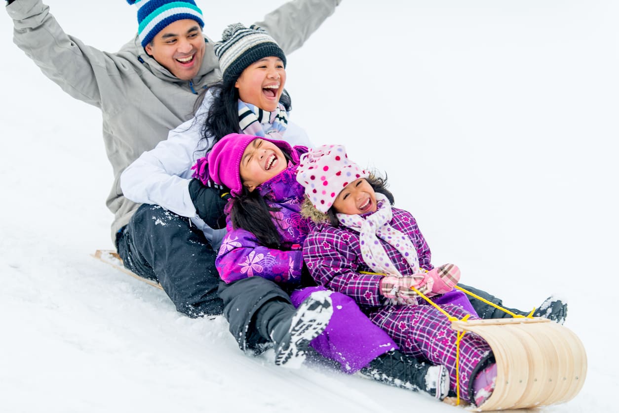 A cheerful family bundled up in winter gear laughs together as they sled down a snowy hill, embracing the spirit of Family Day.
