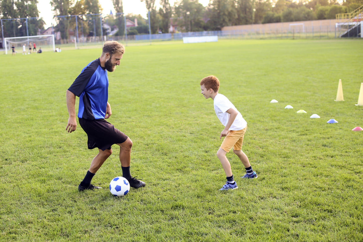 A father and son enjoying a playful soccer match on a sunny day, highlighting their strong bond and quality time together.