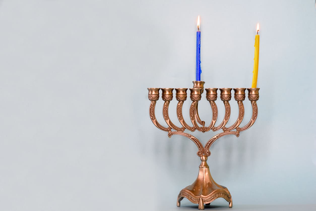 A menorah with two lit candles, including the shamash, symbolizes the First Night of Hanukkah and the beginning of the Festival of Lights.