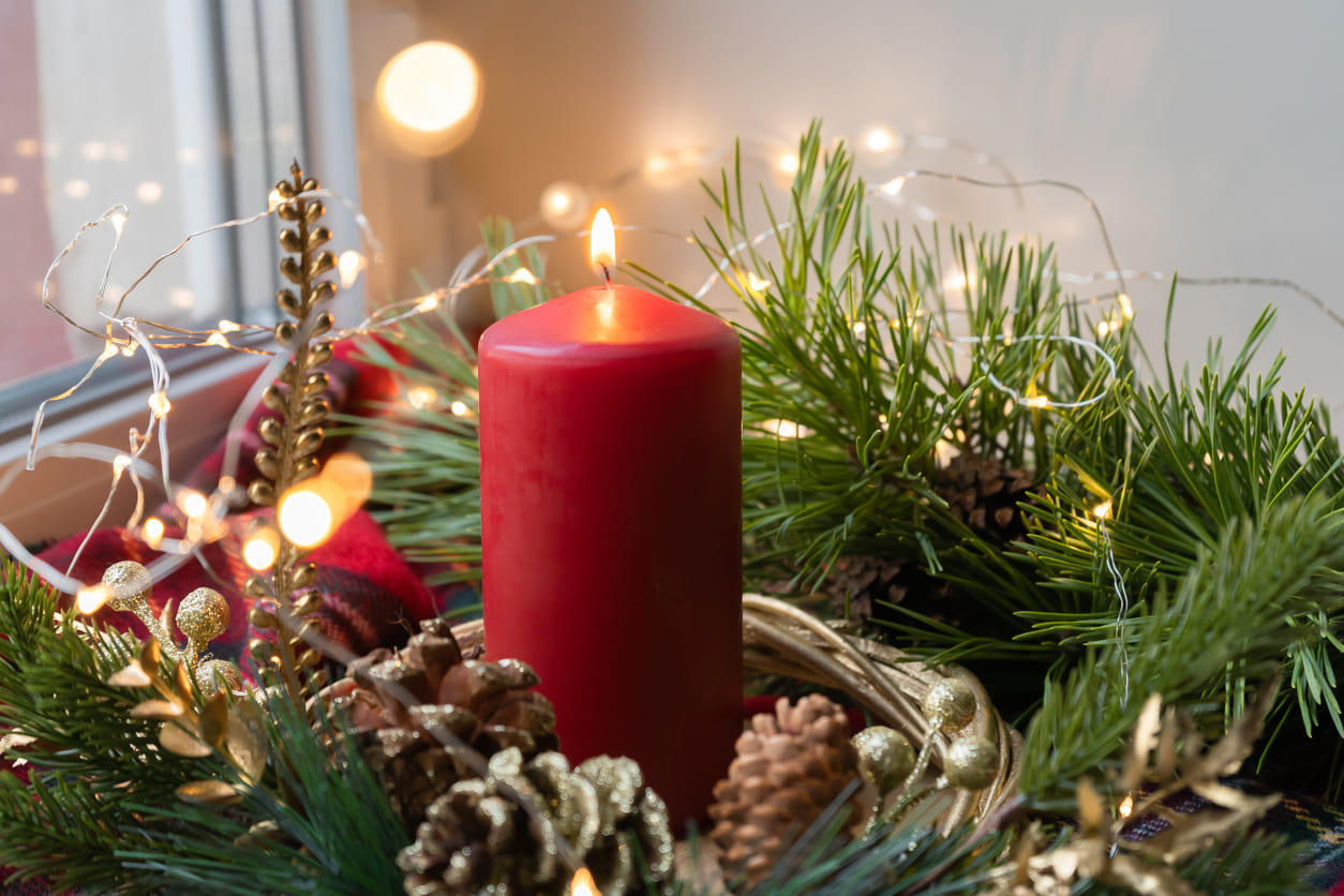 A beautifully lit red Advent candle surrounded by festive greenery and warm lights, symbolizing hope and the start of the Christmas season.