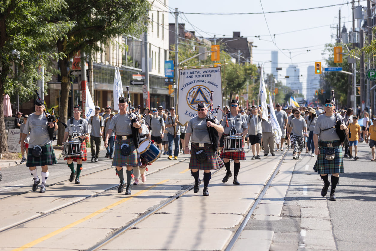 A lively Labour Day parade in Toronto, Canada, with a marching band leading workers and union members in celebration.