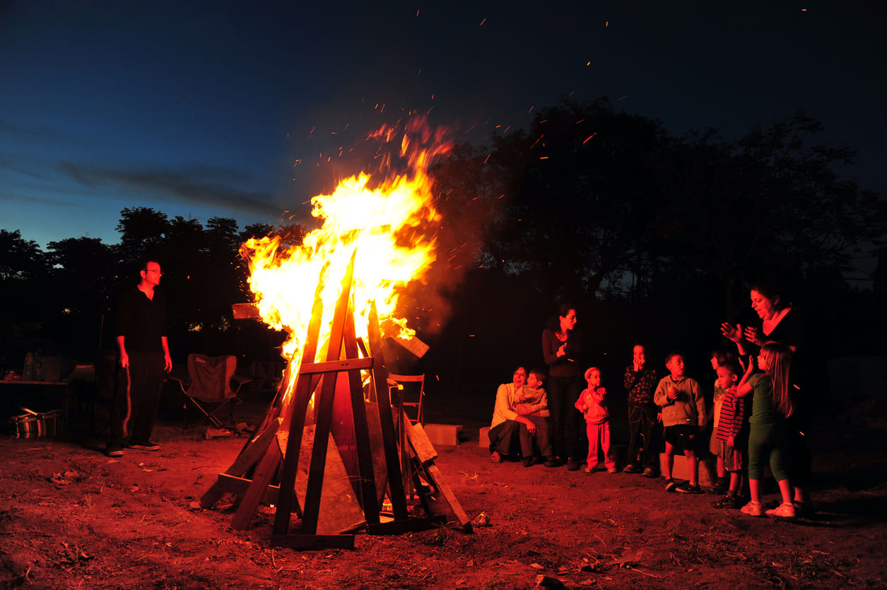 A nighttime scene of a Lag B'Omer celebration, where families and children gather around a large bonfire, enjoying the festive atmosphere.