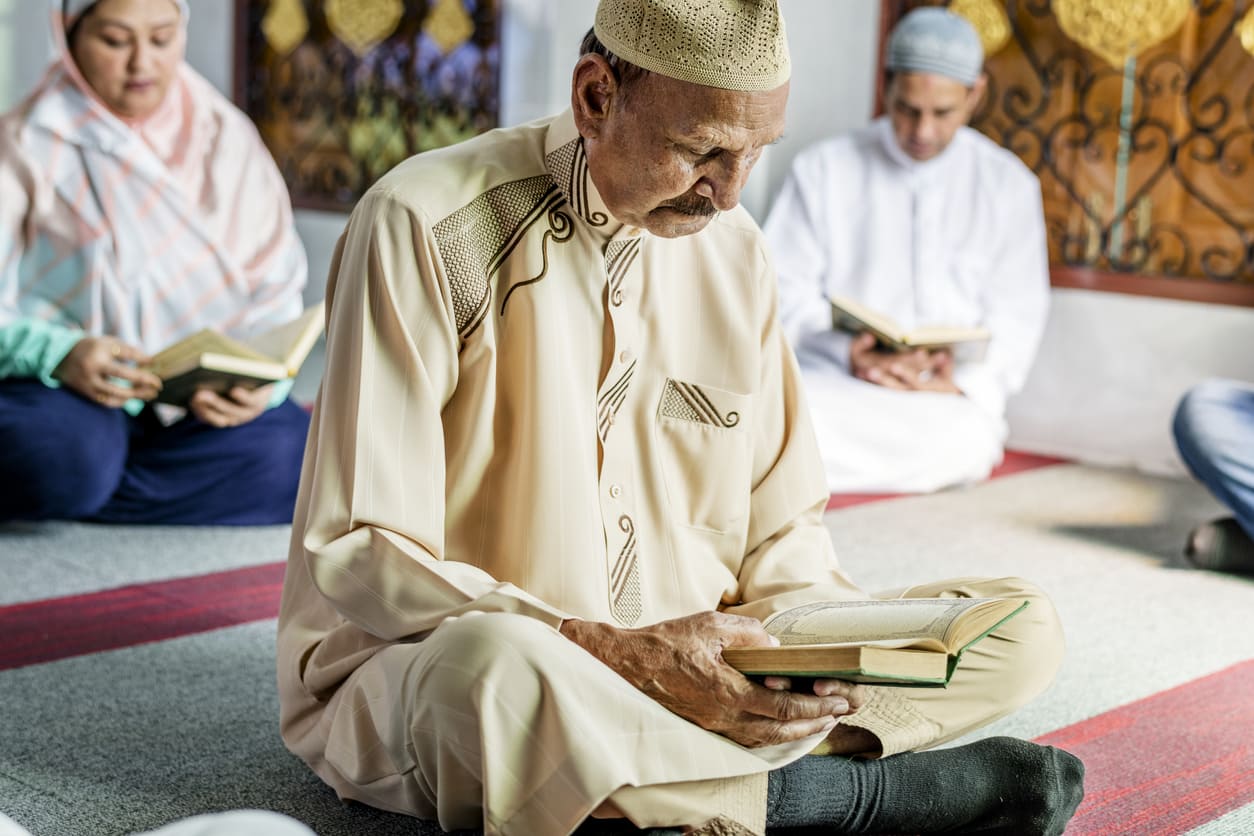 An elderly man and fellow worshippers engage in Quran recitation and prayer, embracing the spiritual essence of Lailat al-Qadr.
