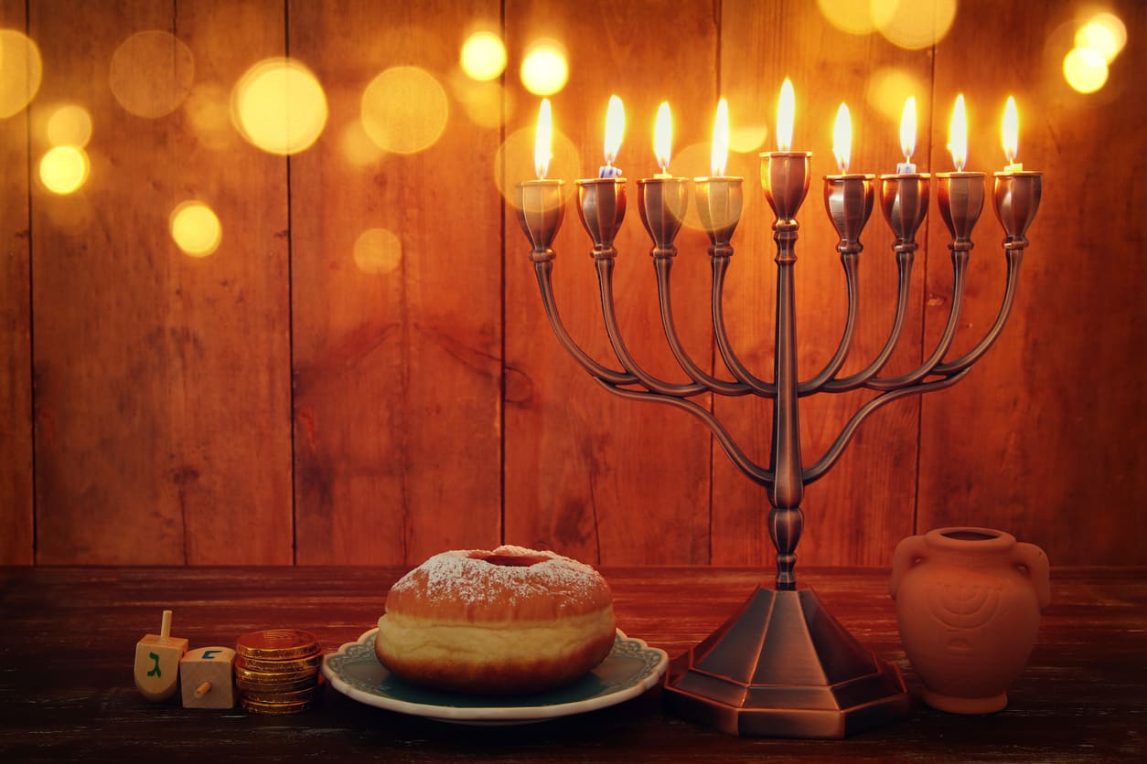 A fully lit menorah, sufganiyah, dreidels, and chocolate coins symbolize the joyous conclusion of Hanukkah on its final night.
