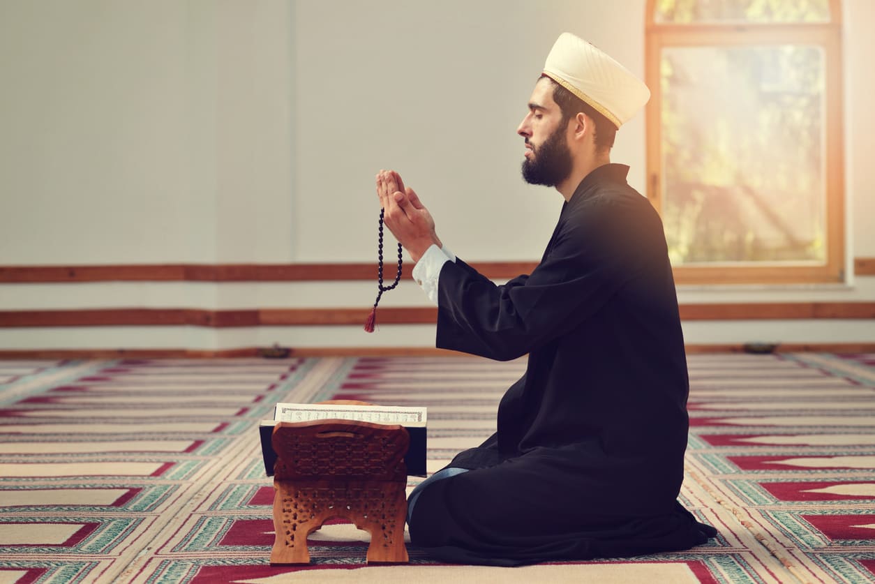 A man sits in quiet devotion, holding prayer beads beside an open Quran, embracing the spiritual essence of Muharram.
